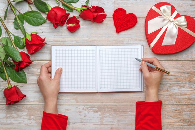 Manos femeninas en mangas rojas listas para escribir en un cuaderno a cuadros de tapa dura escrita