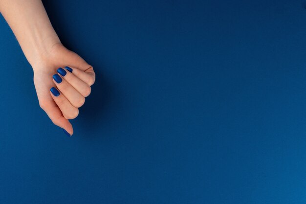 Manos femeninas con manicura de color azul clásico sobre fondo azul. De cerca