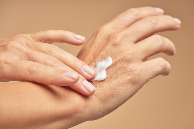 Manos femeninas con manicura desnuda en las uñas aplicando crema de manos