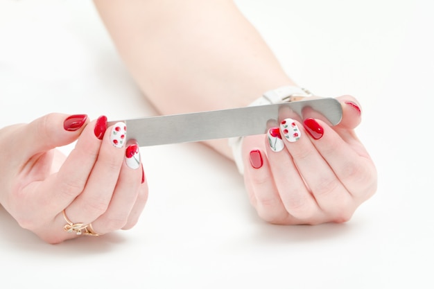 Manos femeninas con manicura, esmalte de uñas rojo, lima de uñas en la mano.