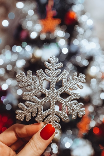 Manos femeninas con manicura francesa sosteniendo un copo de nieve de juguete de Navidad plateado luces de año nuevo bokeh