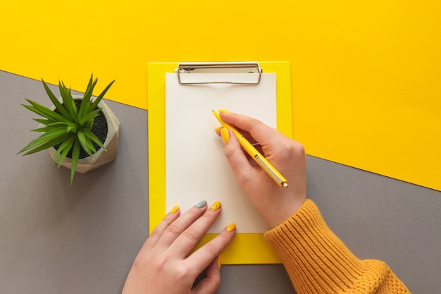 Manos femeninas con manicura fresca escribiendo en papel mesa de oficina escritorio moderno colores amarillo y gris