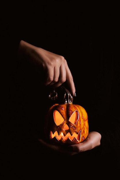 Manos femeninas con manicura negra sostienen linterna de gato de calabaza de cerámica sobre fondo negro