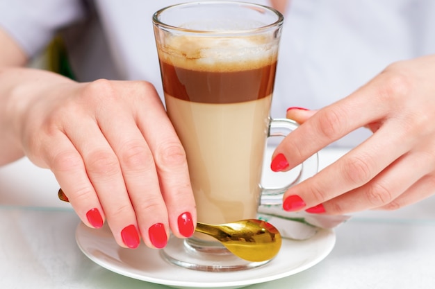 Manos femeninas con manicura roja perfecta sostiene una taza de café capuchino de cerca.