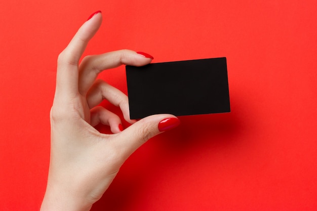 Manos femeninas con manicura roja tiene una tarjeta de presentación en blanco negro