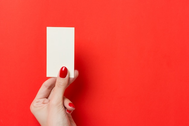 Manos femeninas con manicura roja tiene una tarjeta de visita en blanco blanca