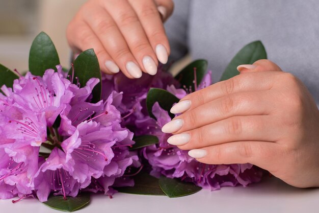 Manos femeninas con manicura romántica uñas esmalte de gel blanco sobre fondo de flores