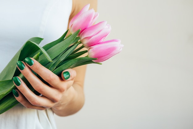 Manos femeninas con la manicura verde que sostiene tulipanes rosados en un fondo beige