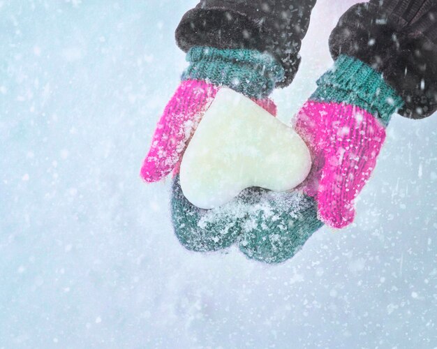 manos femeninas en mitones de punto con corazón de nieve en día de invierno. Concepto de amor.