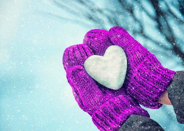 Foto manos femeninas en mitones de punto con corazón de nieve en día de invierno. concepto de amor.