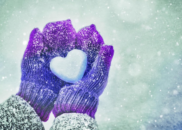 Foto manos femeninas en mitones de punto con corazón de nieve en día de invierno. concepto de amor.