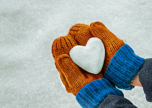 Manos femeninas en mitones tejidos con corazón de nieve en el día de invierno.