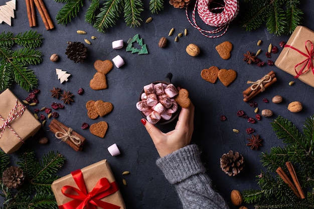 Manos femeninas de Navidad con cajas de regalo y taza de cacao