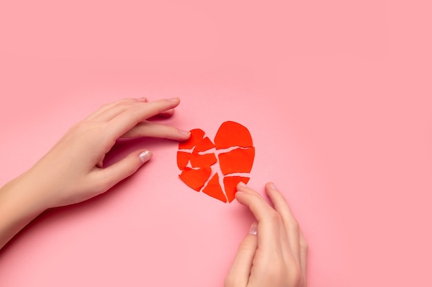 Manos femeninas pegando juntos corazón roto, pedazos de San Valentín rojo roto en rosa