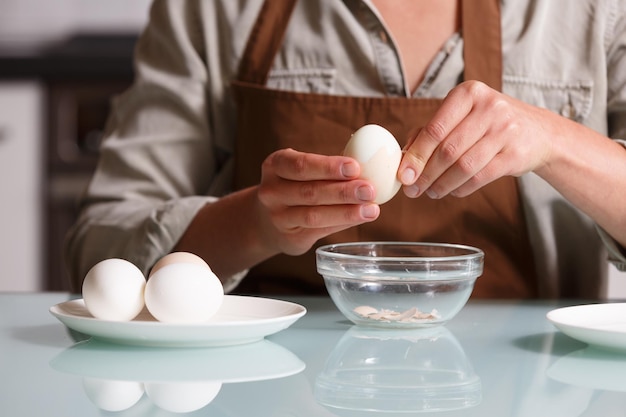 Manos femeninas pelando la cáscara de huevo cocido en una mesa de cocina sobre un plato de vidrio Preparación de huevos cocidos y concepto de nutrición