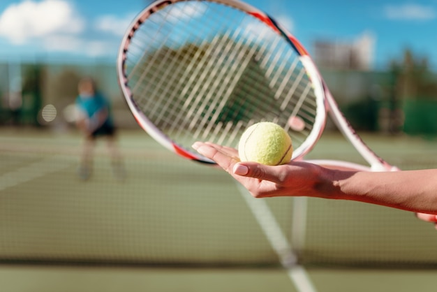 Manos femeninas con pelota y raqueta de tenis, jugador en la cancha.