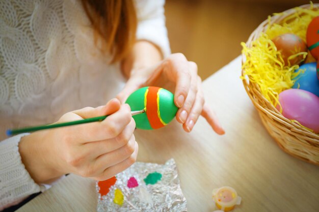 Manos femeninas pintando huevos de Pascua en la mesa en el interior