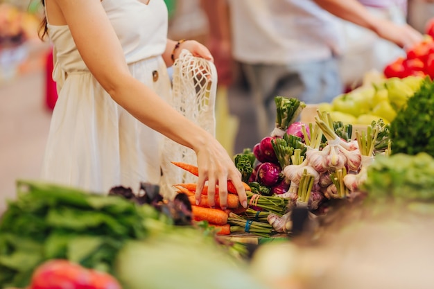 Las manos femeninas ponen frutas y verduras en una bolsa de productos de algodón en el mercado de alimentos. Bolsa ecológica reutilizable para compras. Concepto de desperdicio cero.