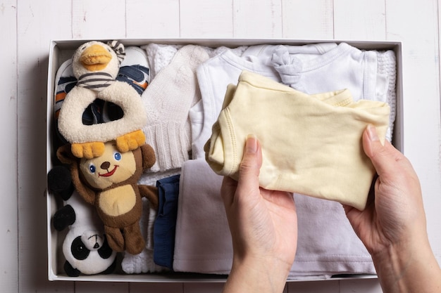 Las manos femeninas ponen ropa, zapatos y juguetes para niños en la caja de donación Concepto de reutilización de reciclaje de ropa de segunda mano