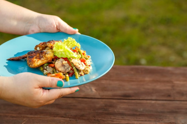 Las manos femeninas ponen sobre la mesa de la calle un plato con pollo y verduras junto a un plato con pollo a la parrilla