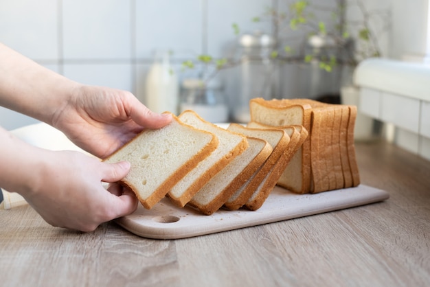 Manos femeninas poniendo rebanadas de pan tostado blanco en la mesa de la cocina