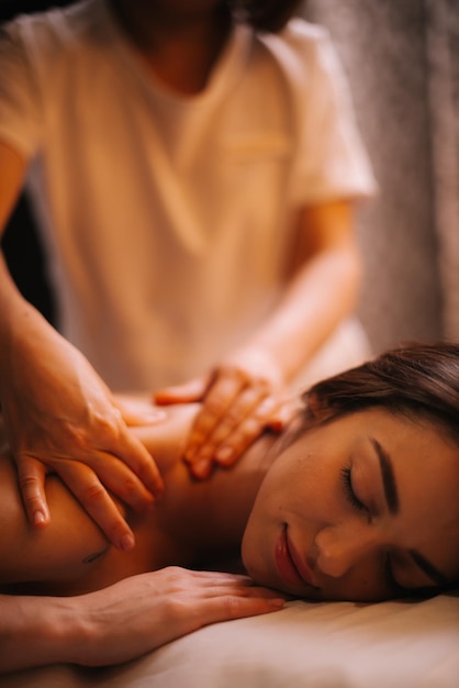 Manos femeninas profesionales dando masaje de espalda a una joven morena en el salón de spa con iluminación suave, primer plano. Concepto de masaje profesional de lujo. Concepto de cuidado del cuerpo.