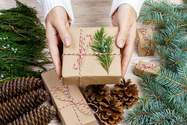 Manos femeninas que envuelven regalos de Navidad en papel y los atan con hilos rojos