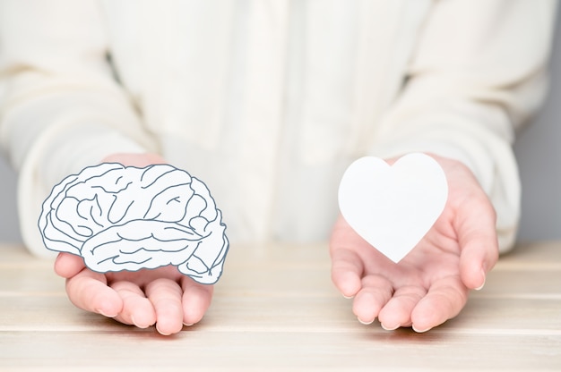 Foto manos femeninas que sostienen el cerebro y el alma de corte de papel. conflicto entre emociones y pensamiento racional. equilibrio y equilibrio entre el concepto de mente y corazón.