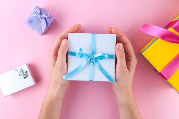 Manos femeninas que sostienen una pequeña caja de regalo blanca envuelta con cinta azul. Para dar y recibir regalos de seres queridos.