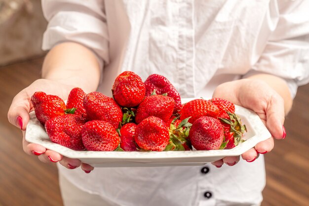 Manos femeninas que sostienen la placa con sabrosas fresas