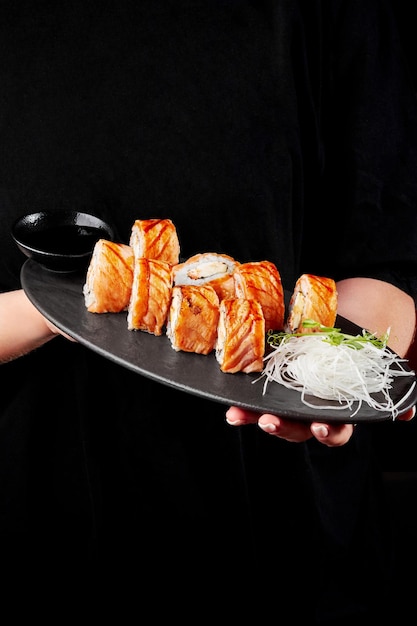 Manos femeninas que sostienen el plato con rollos de sushi con salmón braseado