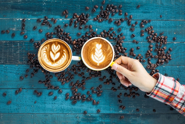 Manos femeninas que sostienen las tazas con los granos de café en fondo de madera del grunge azul