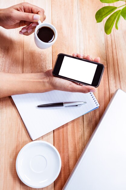 Manos femeninas que sostienen el teléfono inteligente y el café espresso negro