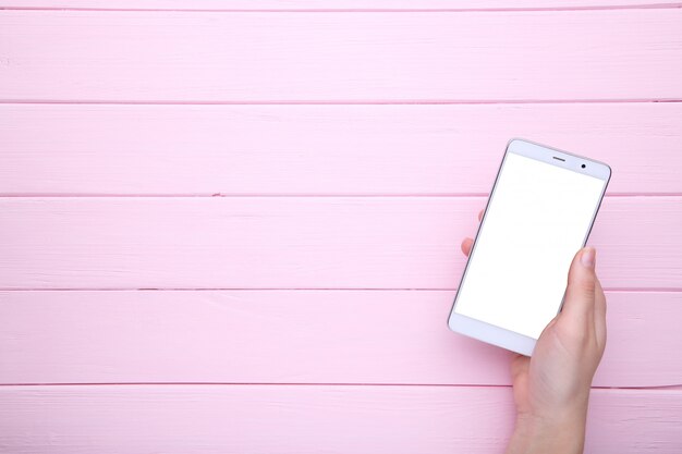 Manos femeninas que sostienen el teléfono móvil con la pantalla en blanco en la madera rosada, Smartphone en la tabla de madera.