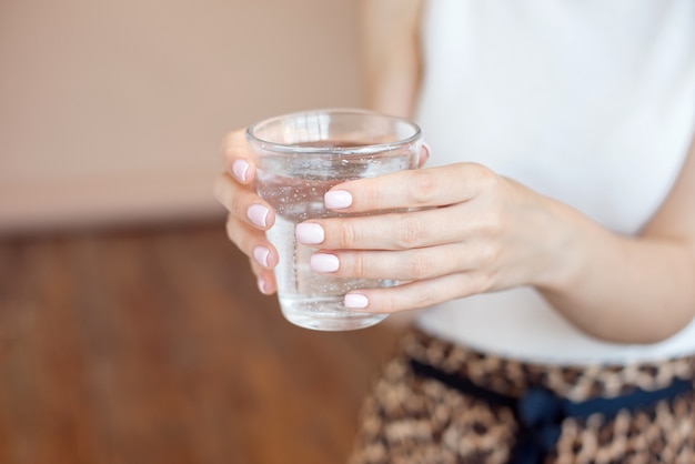 Manos femeninas que sostienen un vaso claro de agua. Un vaso de agua mineral limpia en manos, bebida sana.