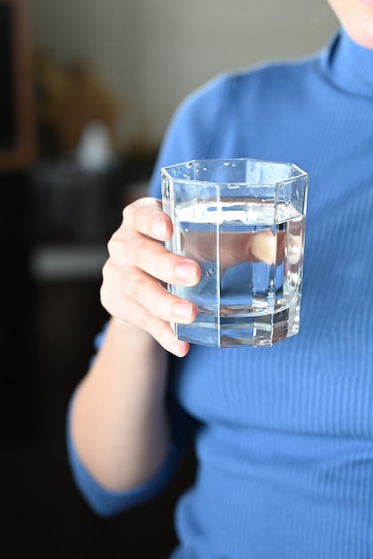 Manos femeninas que sostienen un vidrio claro de agua. Un vaso de agua mineral limpia en las manos, bebida saludable durante la enfermedad.