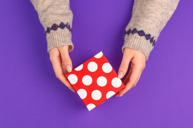 Manos femeninas con regalo envuelto en púrpura