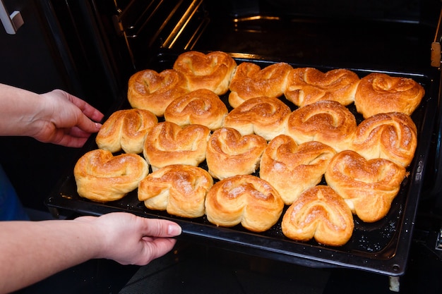 Manos femeninas sacan del horno una bandeja para hornear con bollos caseros.