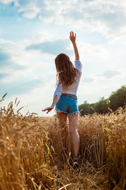 Manos femeninas sobresalen del campo de trigo mujer joven feliz está libre en un campo de trigo dorado maduro n ...