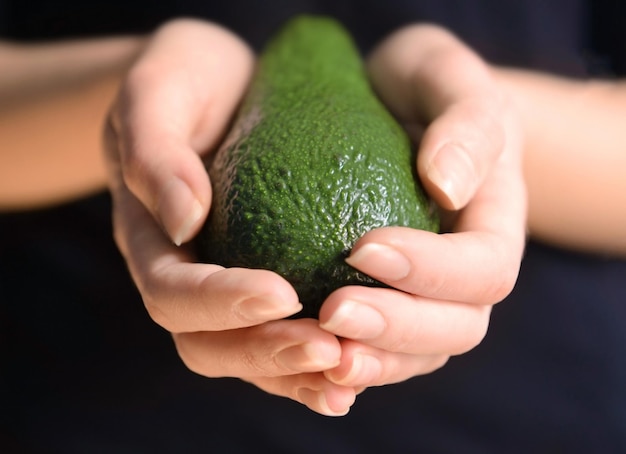 Manos femeninas sosteniendo aguacate sobre fondo negro