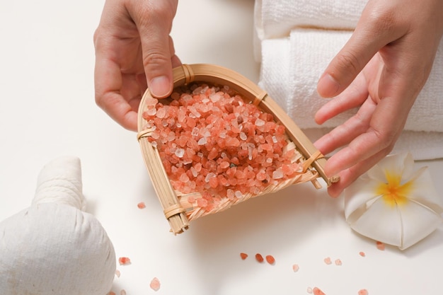 Manos femeninas sosteniendo una bandeja de sal rosa del Himalaya en una mesa de spa blanca minimalista Tratamiento de spa