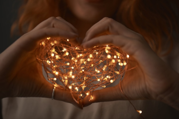 Manos femeninas sosteniendo una cadena de luces en forma de corazón