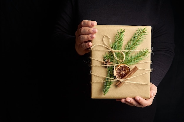 Manos femeninas sosteniendo caja de regalo de Navidad sobre negro