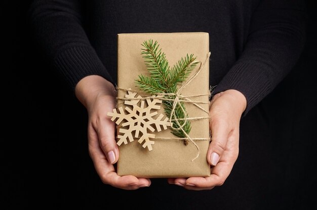 Manos femeninas sosteniendo caja de regalo de Navidad sobre negro