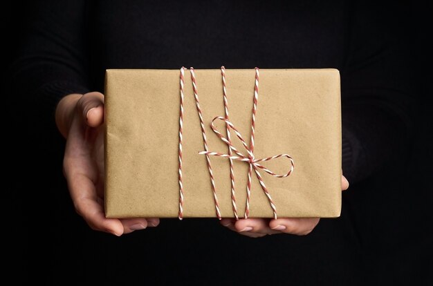 Manos femeninas sosteniendo caja de regalo de Navidad sobre negro