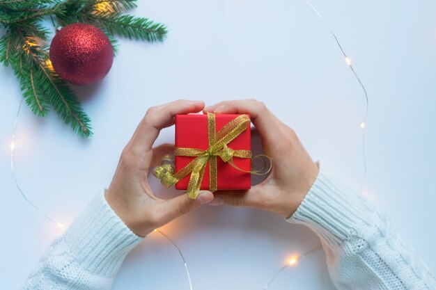 Foto manos femeninas sosteniendo una caja de regalo roja atada con una cinta dorada. concepto de regalos para navidad y año nuevo.