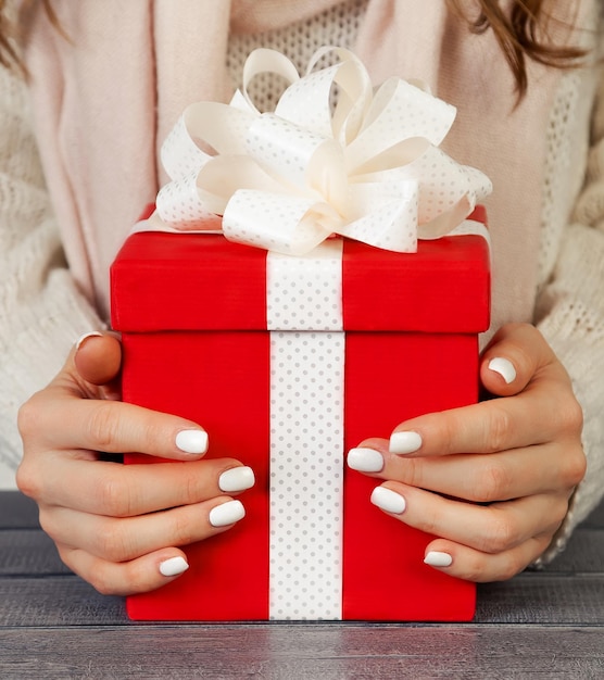 Manos femeninas sosteniendo una caja de regalo roja con una cinta blanca christm