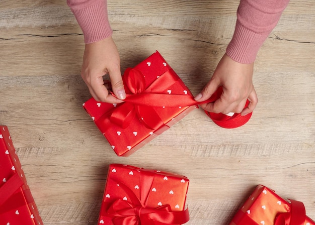 Foto manos femeninas sosteniendo una caja de regalos con una cinta roja sobre un fondo marrón vista desde arriba