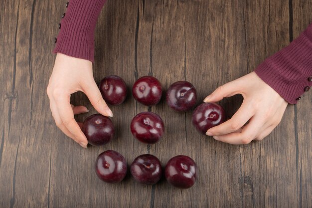 Manos femeninas sosteniendo ciruelas frescas púrpuras sobre superficie de madera.