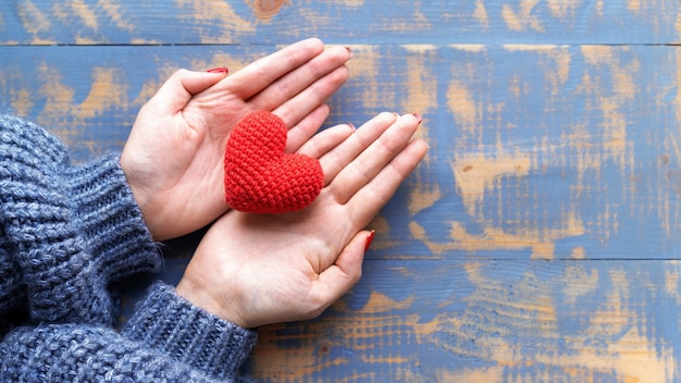 Manos femeninas sosteniendo un corazón rojo tejido a mano. Vista superior